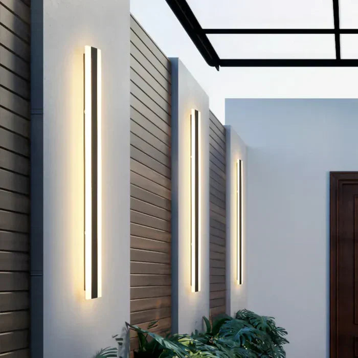 Row of sleek vertical outdoor wall lamps mounted on pillars along a garden walkway