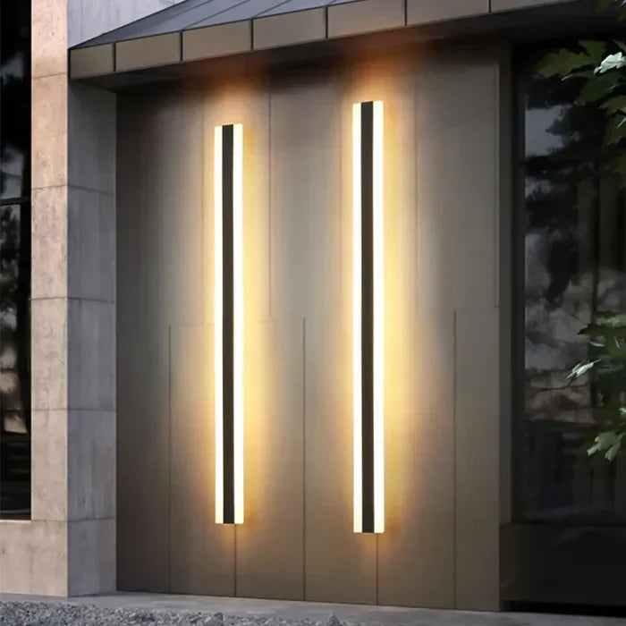 Two modern vertical outdoor wall lamps emitting warm light on a dark building exterior