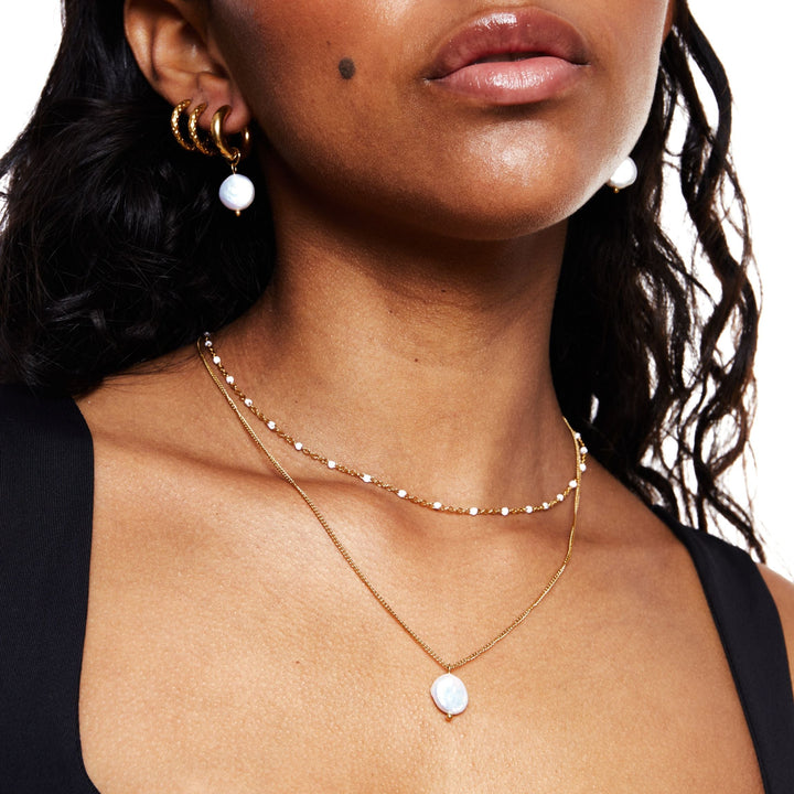 A woman wearing the white enamel bead choker and matching drop earrings against a dark background.