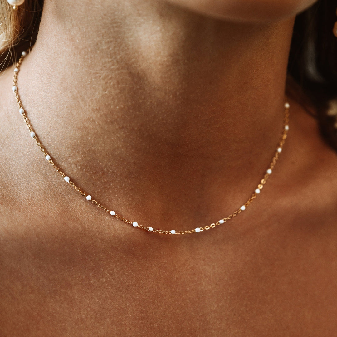 Close-up of a woman wearing a delicate gold choker with white enamel beads around her neck.