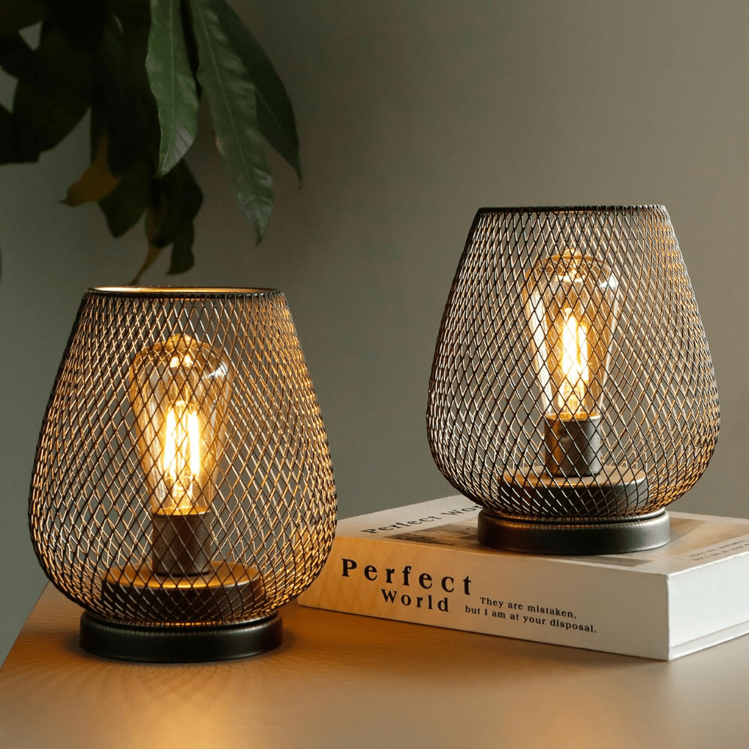 A sleek wireless LED table lantern resting next to a decorative book and green foliage.