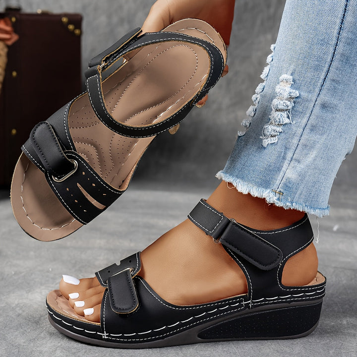 Woman holding black orthopedic comfort sandal with adjustable straps