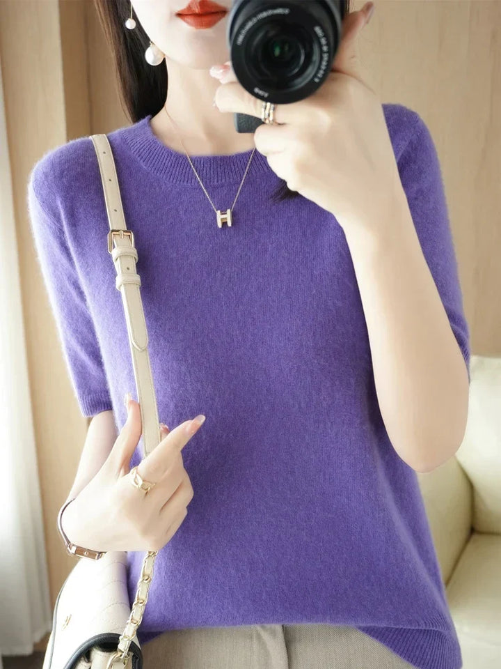 Woman holding a camera while wearing a vibrant purple short-sleeve knit pullover