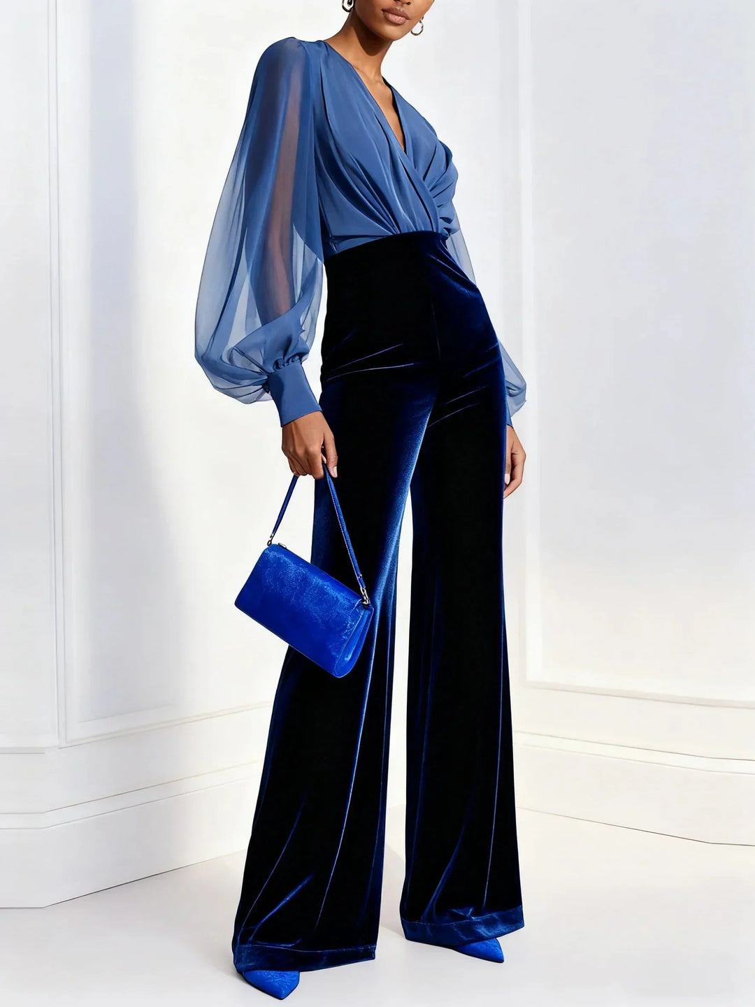 Full-length side angle of a woman modeling a blue velvet wide-leg jumpsuit with elegant bishop sleeves
