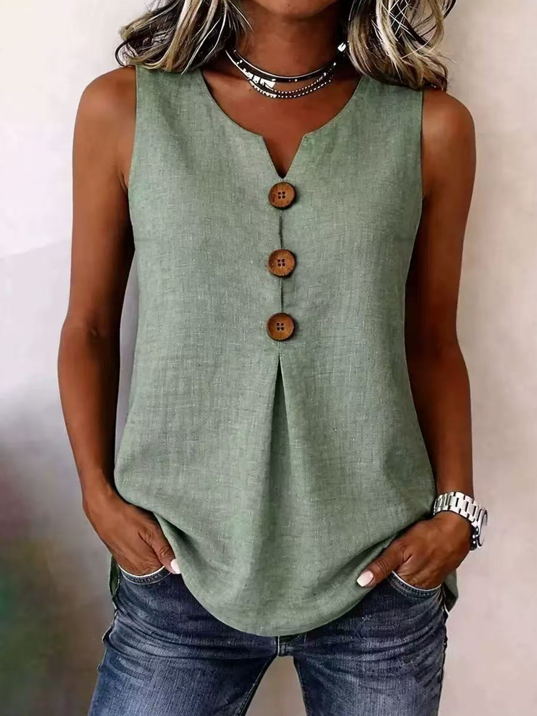 Woman wearing a sage green sleeveless V-neck blouse with front pleating