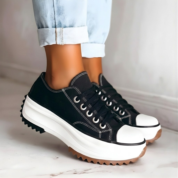 Women's black platform sneakers with chunky white lug soles paired with light jeans