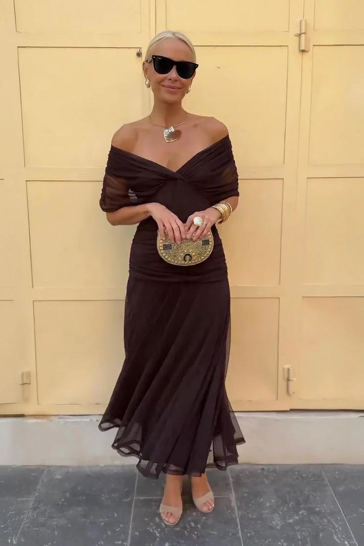 Woman in a dark brown V-neck midi dress holding a small decorative clutch