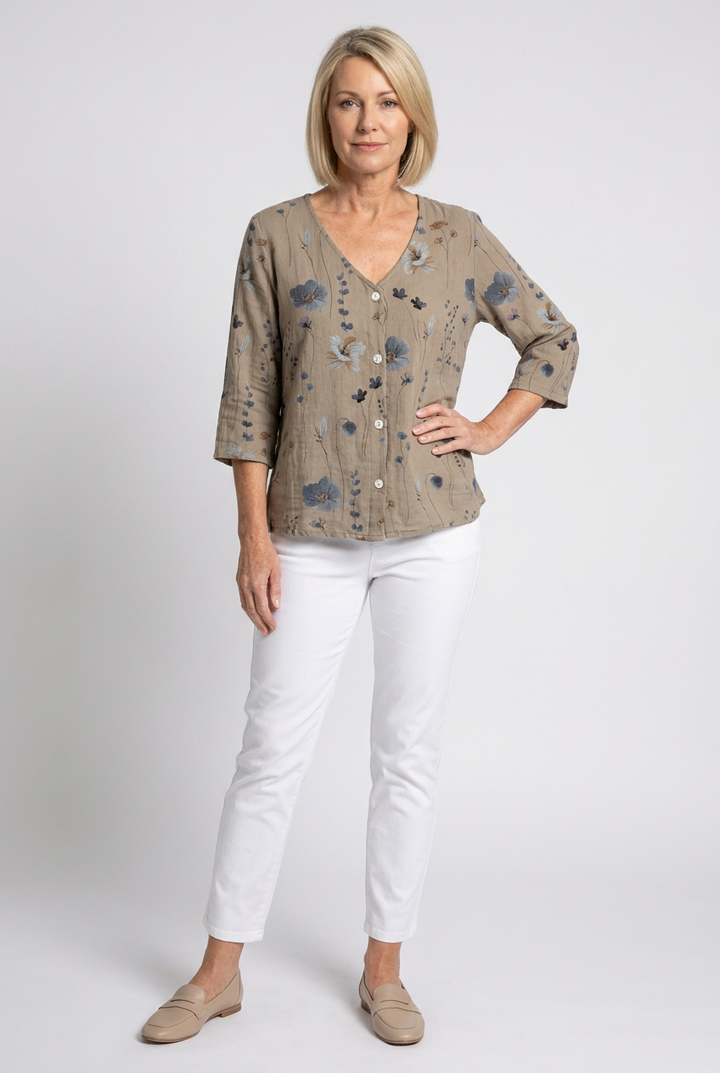 Full-body studio shot of a woman wearing the khaki floral print V-neck blouse and white pants