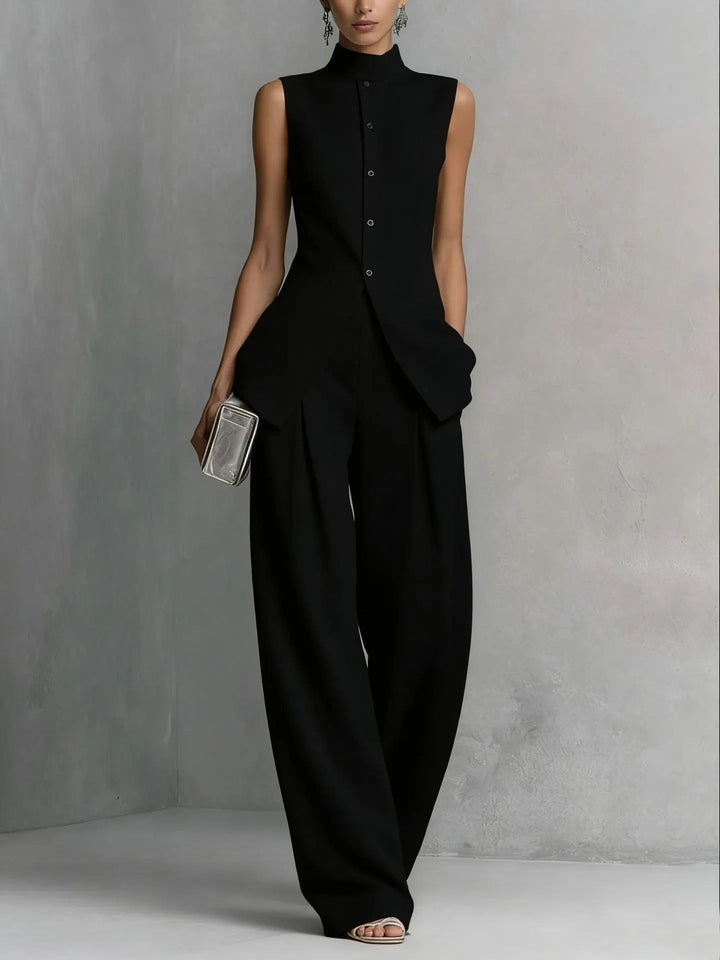 Model wearing a black sleeveless top and matching wide-leg trousers in a minimalist setting