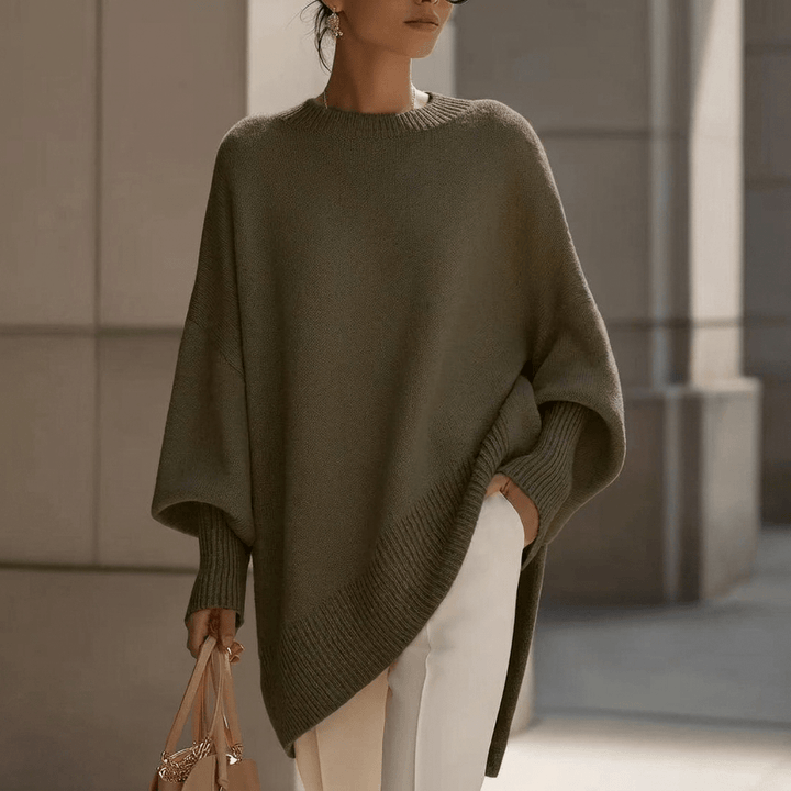 Woman wearing a dark green oversized knit pullover sweater paired with white trousers