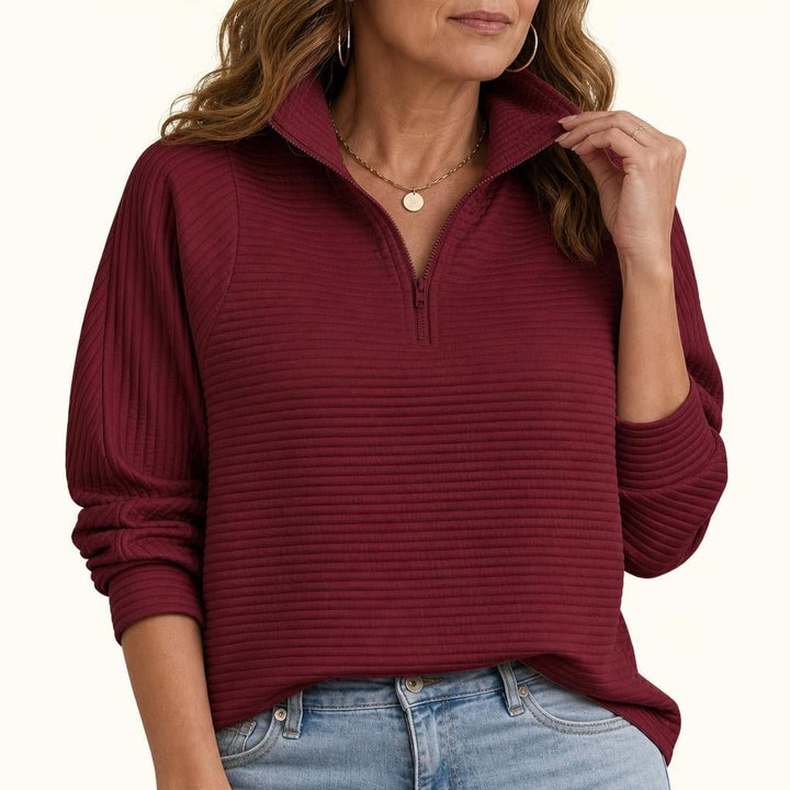 A woman wearing a wine red ribbed half-zip funnel neck sweater with balloon sleeves, paired with blue jeans.