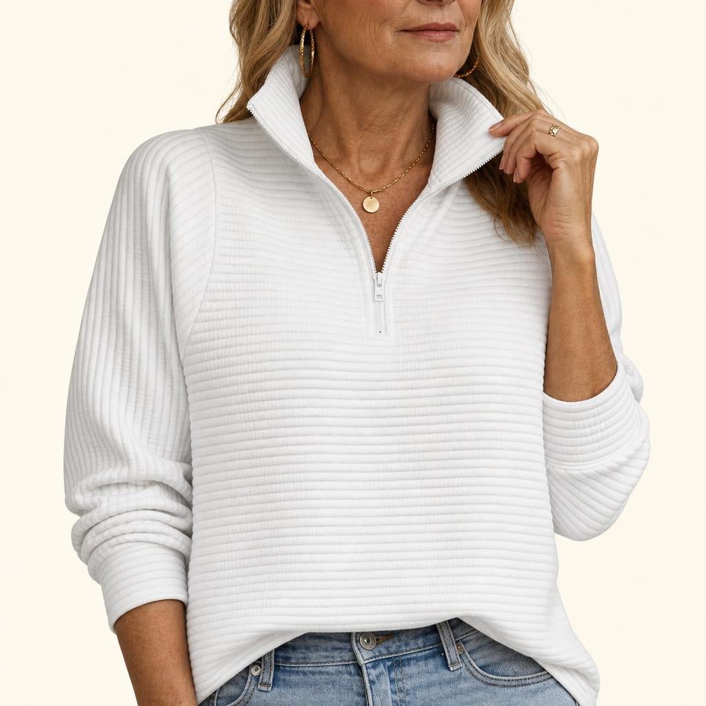 A woman wearing a white ribbed half-zip funnel neck sweater with balloon sleeves, paired with blue jeans.