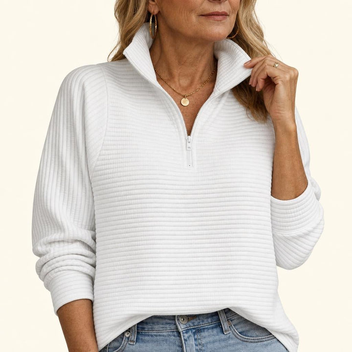 A woman wearing a white ribbed half-zip funnel neck sweater with balloon sleeves, paired with blue jeans.