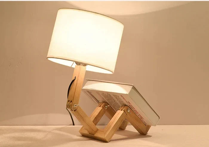 Wooden robot-shaped table lamp holding an open book on a desk